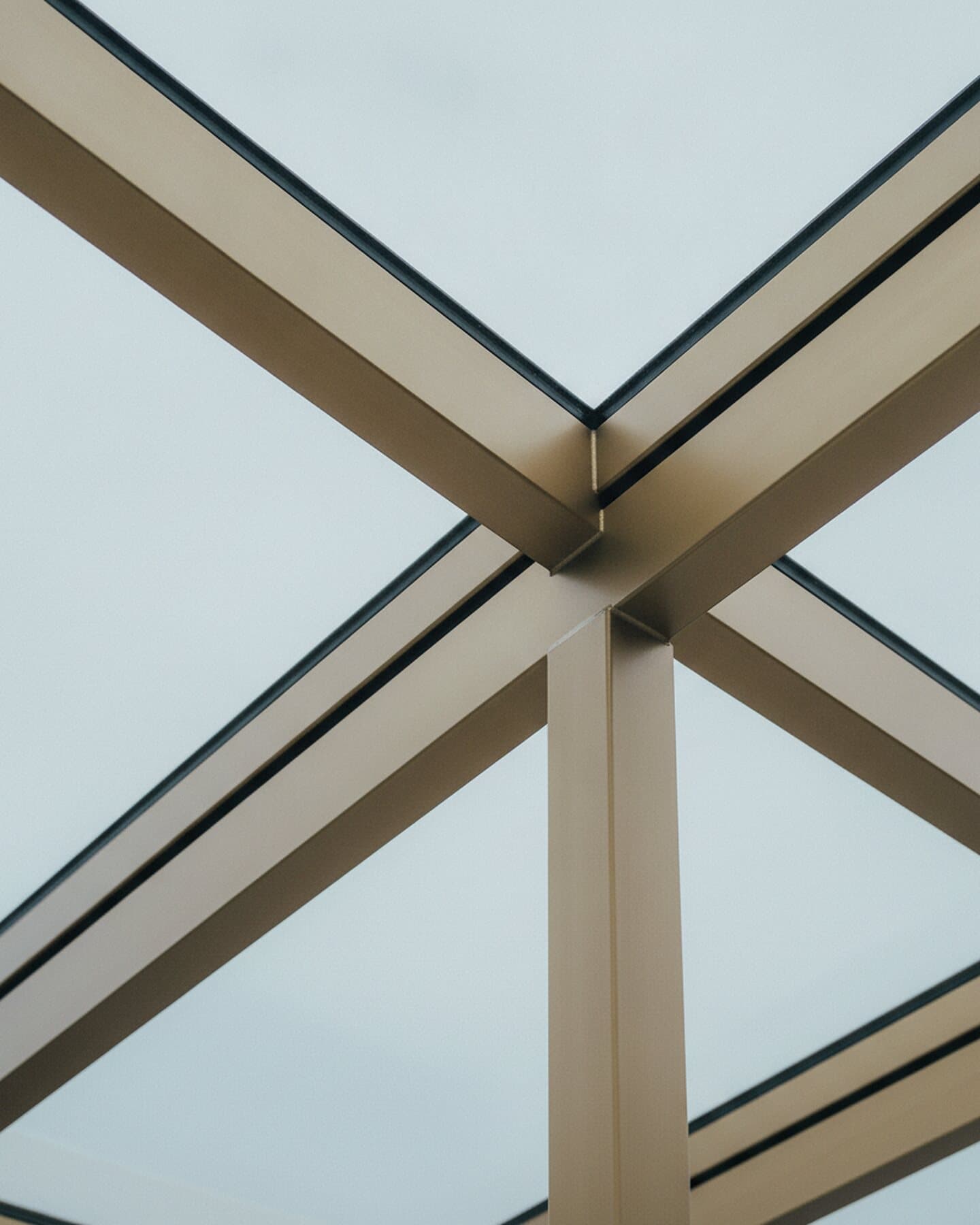 Detail eines Aluminium-Glasdaches: Sprossen und Pfosten vor hellem Himmel